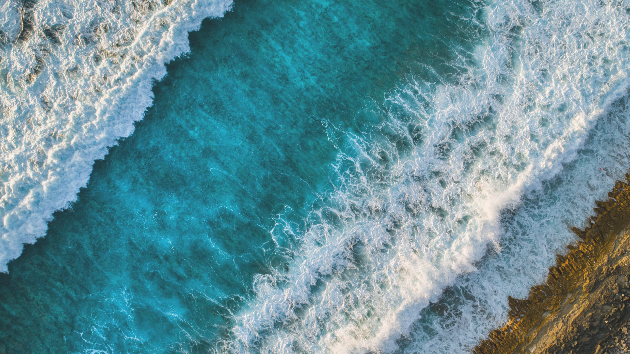 Aerial view of vibrant turquoise waves crashing onto a sandy beach